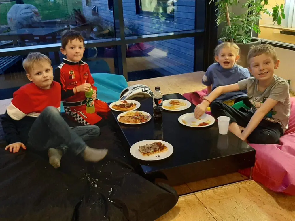 Fire børn hygger sig med pizza og sodavand ved et lavt bord til børnefødselsdag
