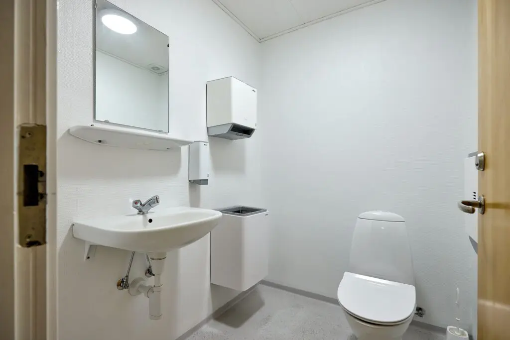 Lyst badeværelse med toilet, håndvask, spejl og papirdispenser hos Kraftværket Videbæk
