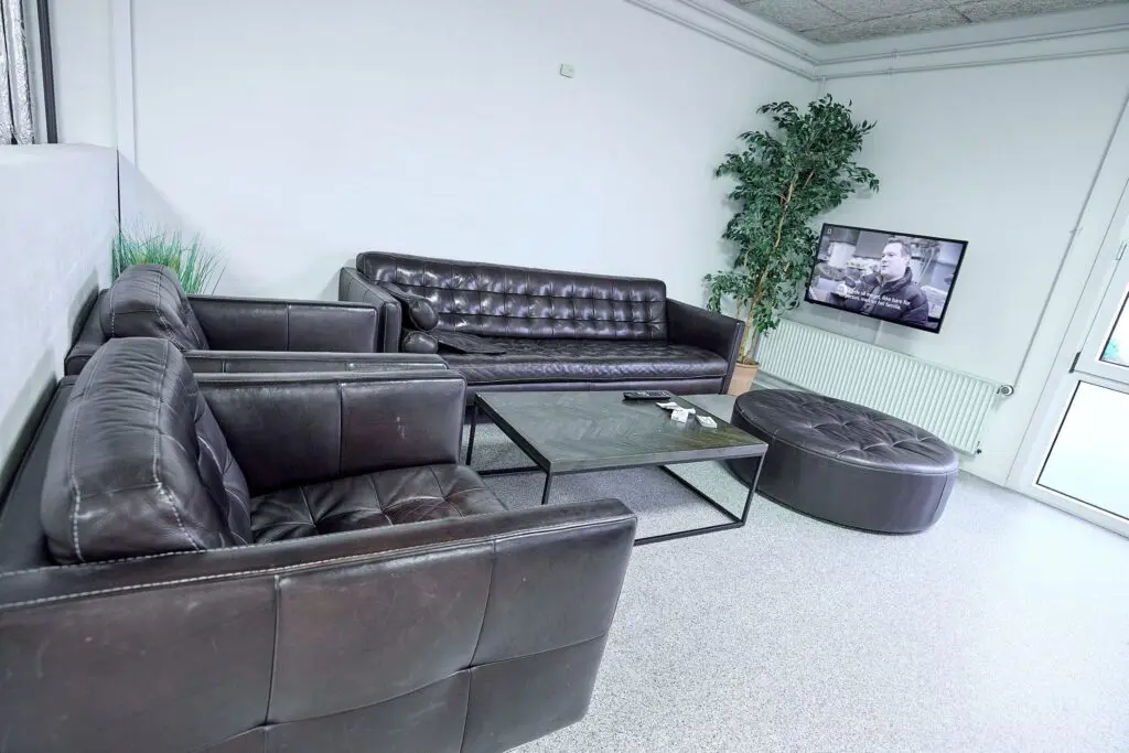Loungeområde med mørke lædersofaer, sofabord og vægmonteret TV i opholdsrum hos Kraftværket Videbæk