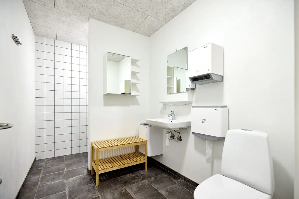 Lyst badeværelse med toilet, håndvask, spejl og træbænk hos Kraftværket Videbæk