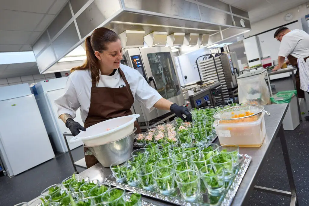 Kok anretter forretter med rejer og salat i glas i et professionelt industrikøkken