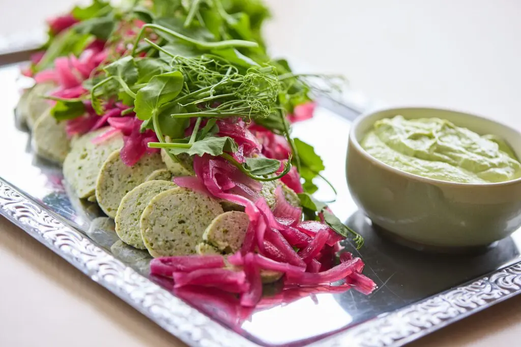 Anretning på sølvfad med skiver af terrine, syltede rødløg, friske urter og en skål grøn dressing