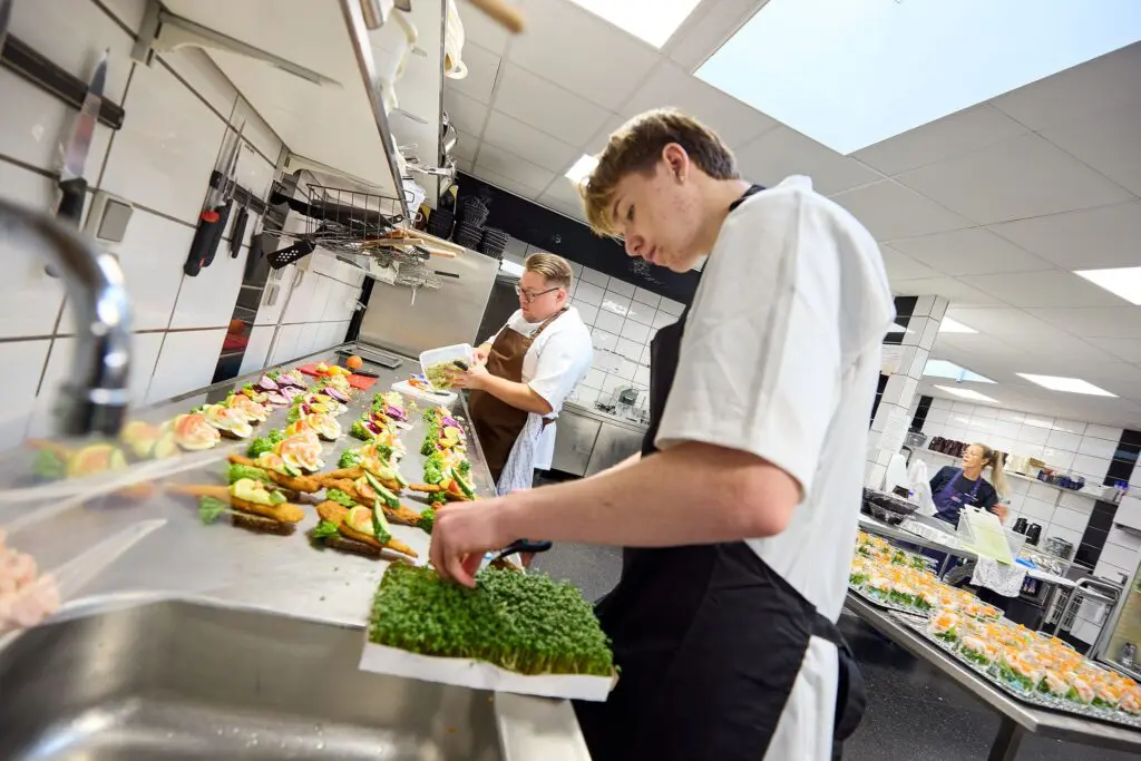 Køkkenpersonale i storkøkken anretter og pynter frisksmurt smørrebrød med karse