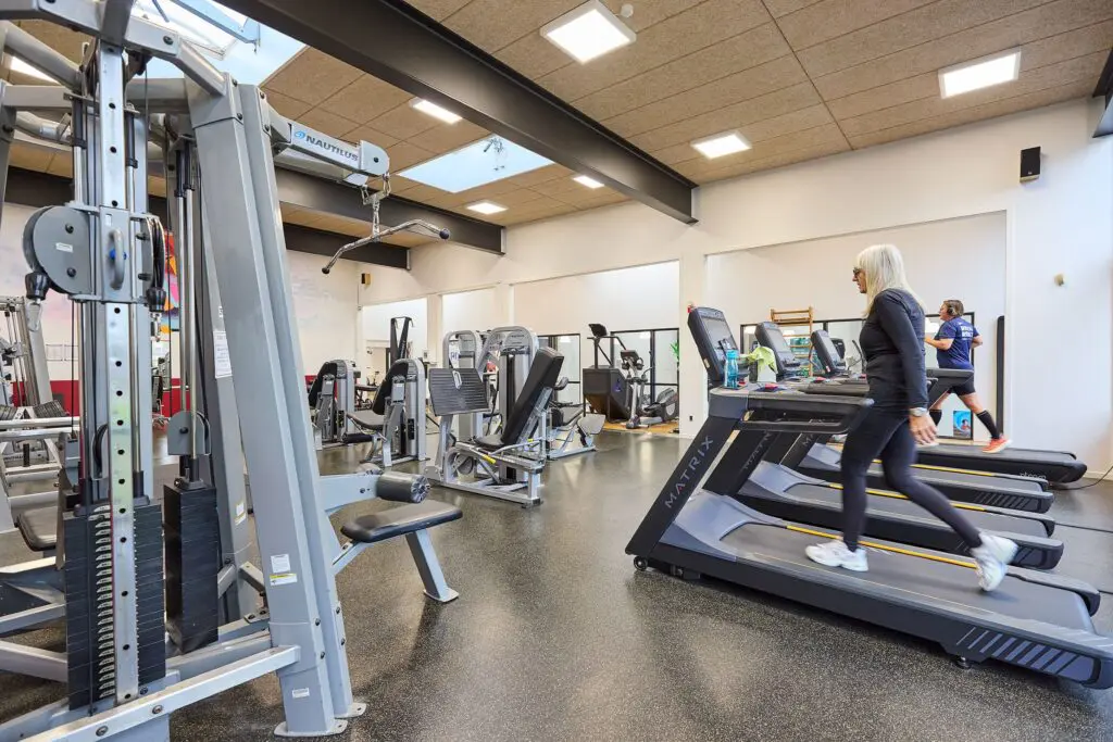 Personer der træner på løbebånd i et lyst fitnesscenter med styrketræningsmaskiner