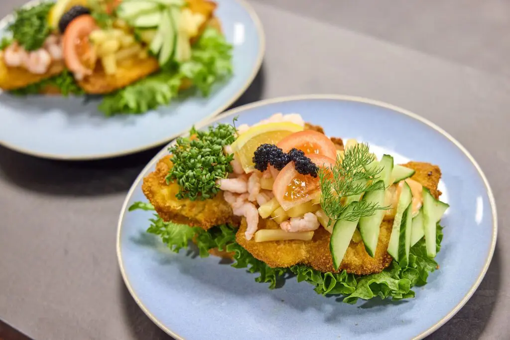 Klassisk stjerneskud med paneret fiskefilet, rejer, kaviar, citron, tomat og agurk anrettet på en blå tallerken