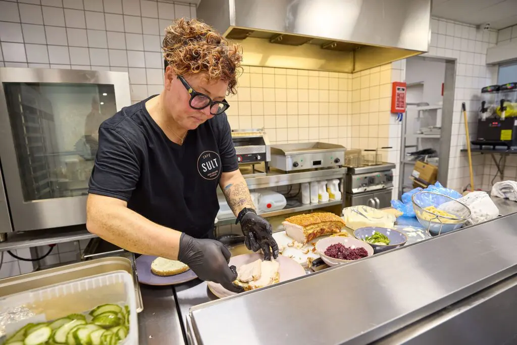 Pernille anretter en flæskestegssandwich med sprøde svær og rødkål i køkkenet hos Café SULT i Kraftværket Videbæk