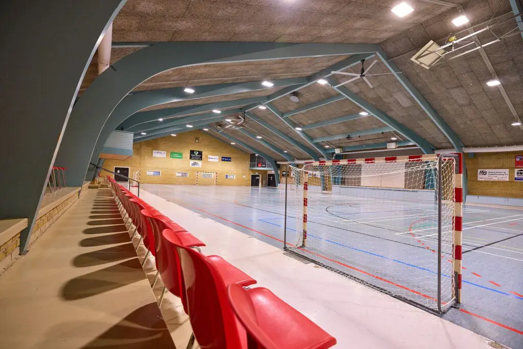 Stor idrætshal i Kraftværket Videbæk med røde tilskuersæder, håndboldmål og opstreget sportsgulv til boldspil
