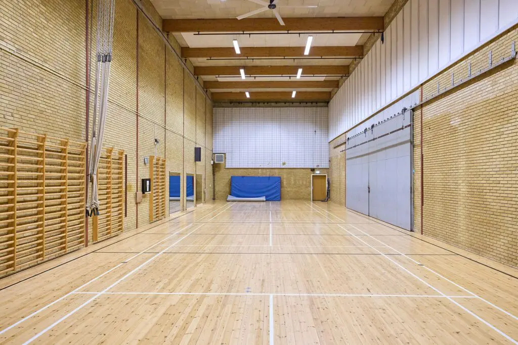 Gymnastiksal med lyst trægulv, opstregede baner, klatretove og ribber på murstensvæg i Kraftværket Videbæk