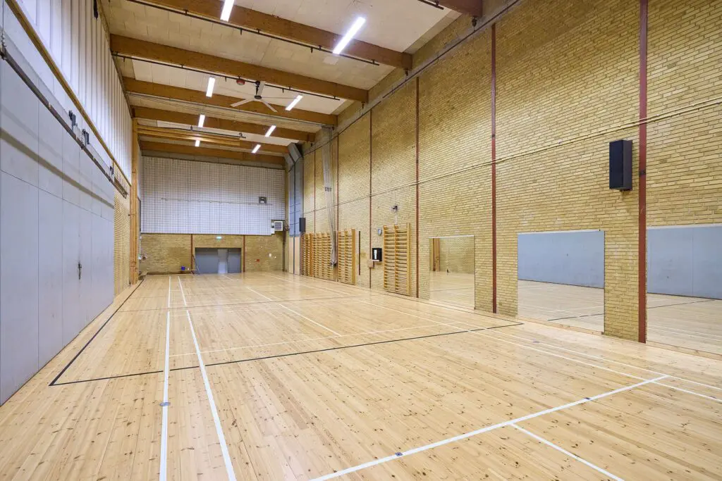 Indendørs gymnastiksal med lyst trægulv, banemarkeringer, ribber og spejle i Kraftværket Videbæk