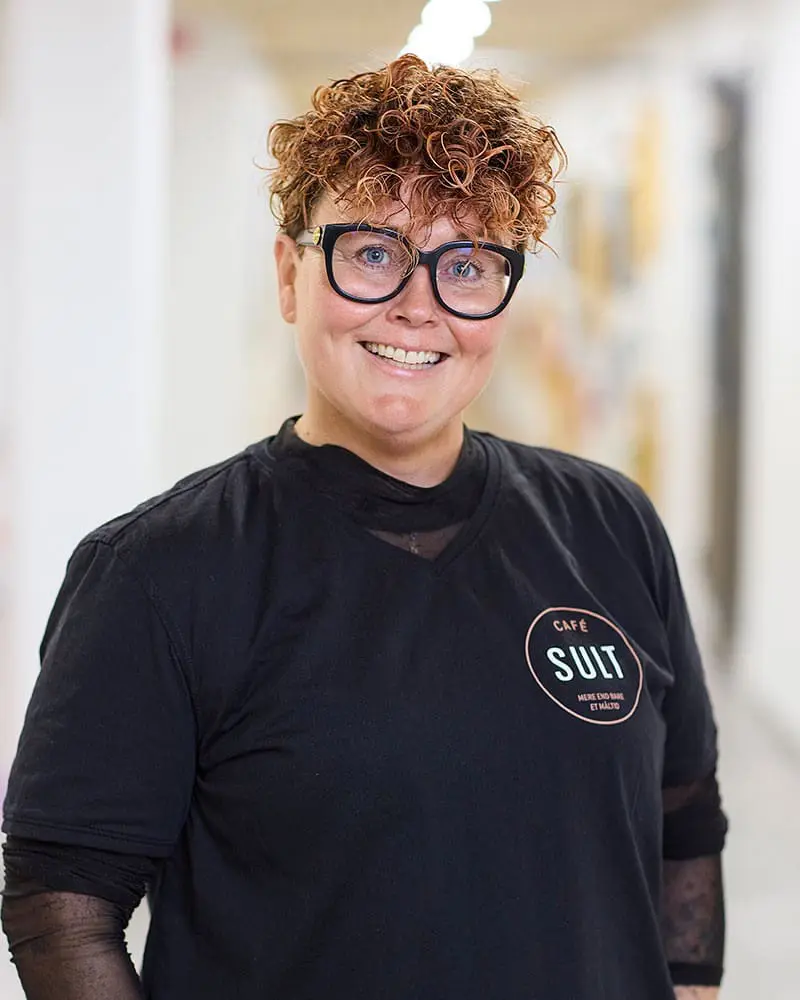 Portræt af smilende Pernille Holmen med briller iført sort Café SULT t-shirt