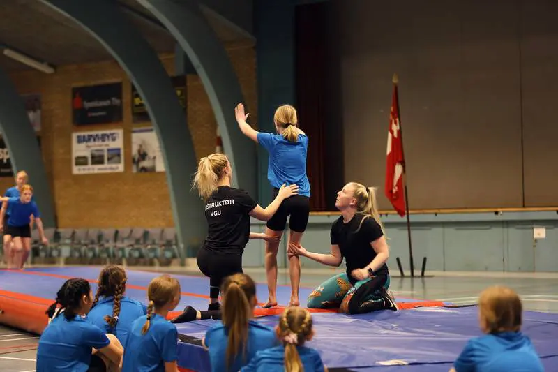 Instruktører hjælper en ung gymnast på airtrack under træning i idrætshallen i Kraftværket Videbæk