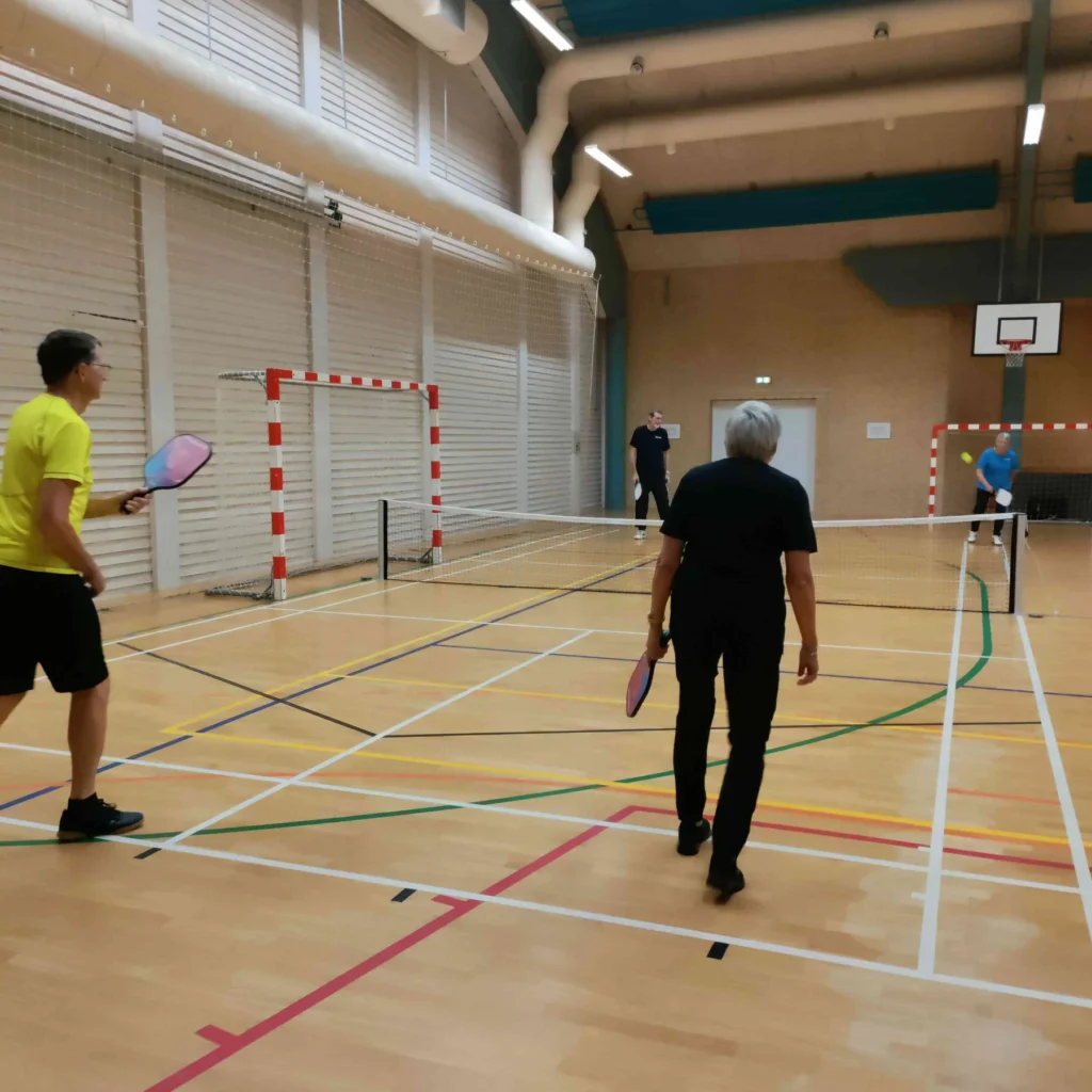 Fire personer spiller pickleball over net i en idrætshal